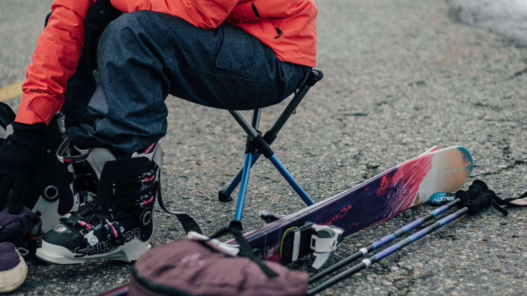 Compact BTR camp stool in snow while someone sits on it to lace their snowboard boots